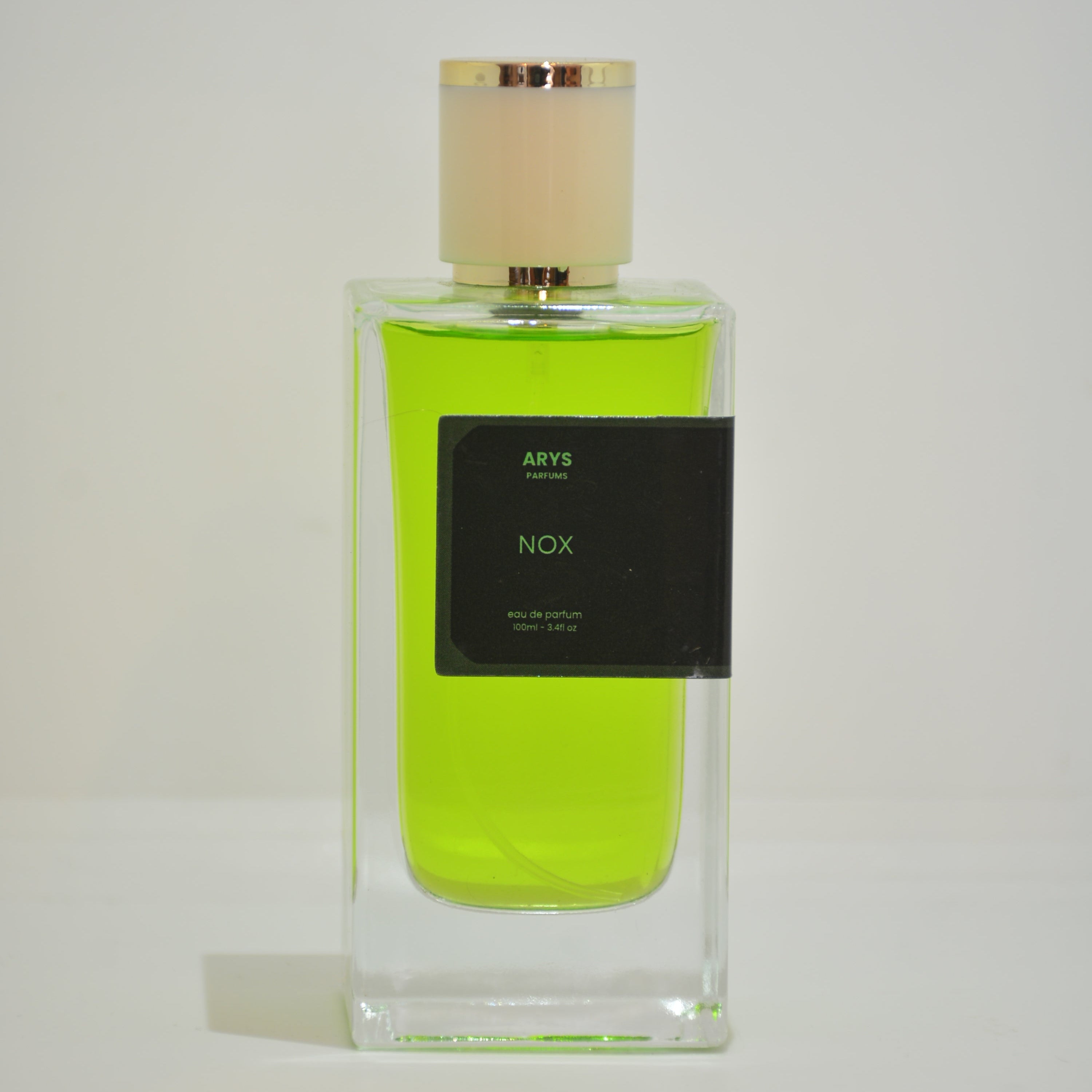 A clear rectangular perfume bottle filled with bright neon yellow-green liquid, featuring a black label with white text and a pale beige cap, shown on a plain light background. This is Nox, inspired from XJ 1861 Naxos by Xerjoff.