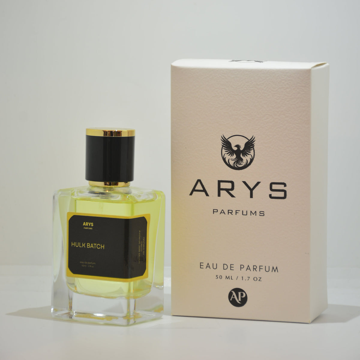A bottle of Arys Parfums with pale yellow liquid and a black cap, shown next to its beige packaging box on a light gray background. This is Hulk Batch, inspired from the 2018 batch of Creed Aventus.